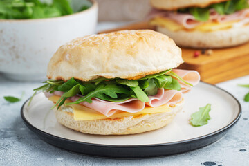 Two homemade sandwiches with ham, cheese and arugula on a concrete table.