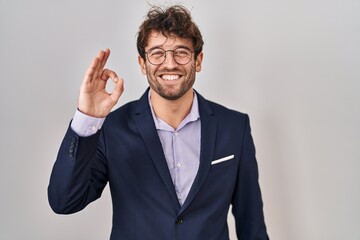 Hispanic business man wearing glasses smiling positive doing ok sign with hand and fingers. successful expression.