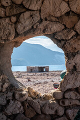 Looking at a stone building through a stone window with beach, ocean and a mountain