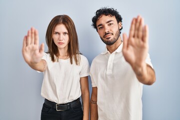 Young couple wearing casual clothes standing together doing stop sing with palm of the hand....