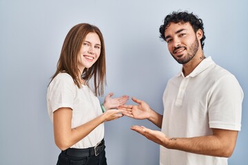 Young couple wearing casual clothes standing together inviting to enter smiling natural with open hand