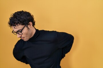 Hispanic man standing over yellow background suffering of backache, touching back with hand, muscular pain