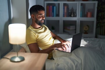 Young arab man using laptop sitting on bed at bedroom