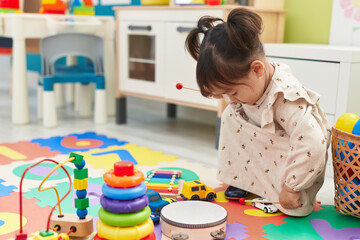 Adorable chinese girl playing drum sitting on floor at kindergarten