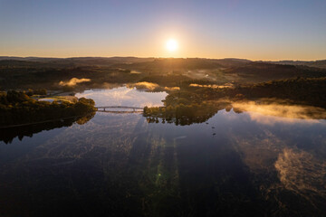 Aerial view of Lac de Saint Pardoux and its footbridge at sunrise in autumn with fog and mirror water