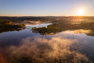 Naklejka na ściany i meble Aerial view of Lac de Saint Pardoux and its footbridge at sunrise in autumn with fog and mirror water