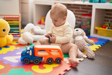 Adorable caucasian baby playing with car and truck toy sitting on floor at kindergarten