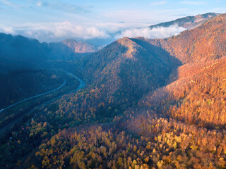 Aerial view of mountain landscape with setting sun: colourful, red beech autumn forest covering the mountains, winding roads and the Váh river in the valley. Strecno area, Slovakia.