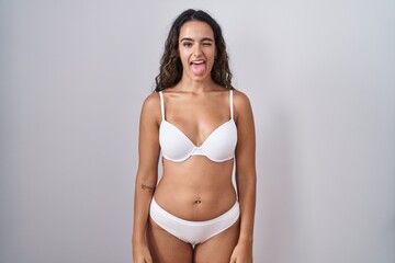 Young hispanic woman wearing white lingerie sticking tongue out happy with funny expression. emotion concept.