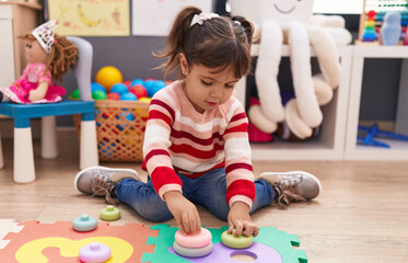 Adorable hispanic girl playing with toys sitting on floor at kindergarten
