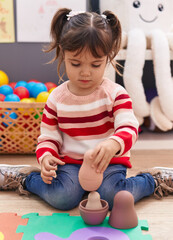 Adorable hispanic girl playing with toys sitting on floor at kindergarten