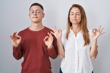 Mother and son standing together over isolated background relaxed and smiling with eyes closed doing meditation gesture with fingers. yoga concept.