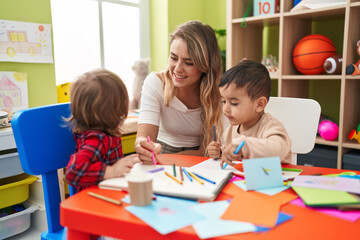 Fototapeta premium Teacher with boys sitting on table drawing on paper at kindergarten