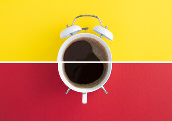 Black coffee on the dial of the white alarm clock on the yellow and red  background. Top view.
