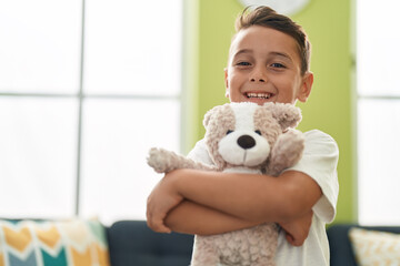Adorable hispanic toddler hugging teddy bear standing at home