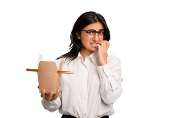 Young business indian woman eating takeaway noodles cut out isolated biting fingernails, nervous and very anxious.