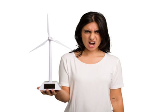 Young Indian woman holding a small wind energy mill isolated screaming very angry and aggressive.