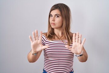 Young hispanic woman standing over isolated background moving away hands palms showing refusal and...