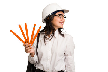 Young architect indian woman with helmet and holding a meter cut out isolated looks aside smiling, cheerful and pleasant.