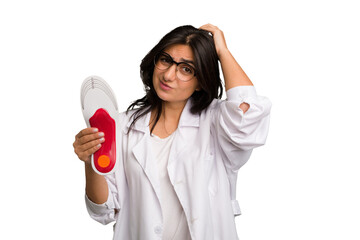 Young indian chiropodist woman holding a insoles for shoes cut out isolated touching back of head,...