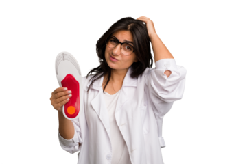 Young indian chiropodist woman holding a insoles for shoes cut out isolated touching back of head, thinking and making a choice.