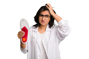 Young indian chiropodist woman holding a insoles for shoes cut out isolated being shocked, she has...