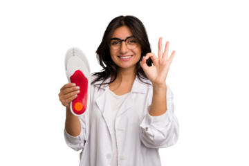 Young indian chiropodist woman holding a insoles for shoes cut out isolated cheerful and confident showing ok gesture.
