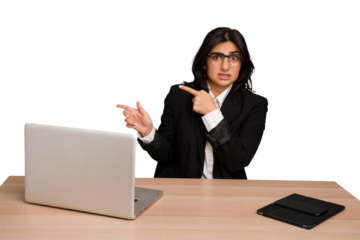 Young indian woman in a table with a laptop and tablet isolated shocked pointing with index fingers to a copy space.