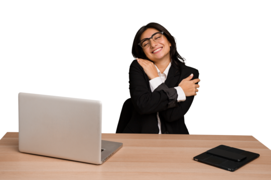 Young indian woman in a table with a laptop and tablet isolated hugs, smiling carefree and happy.