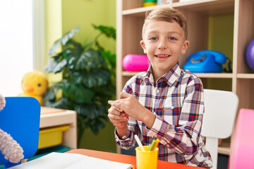Adorable caucasian boy student sitting on table drawing on notebook at kindergarten