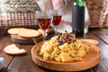 Creamy polenta with porcini mushrooms, bacon, served on a dark wooden background with a glass of red wine. Typical food of northern Italy, Trentino in the Alps 