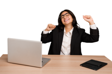 Young indian woman in a table with a laptop and tablet isolated celebrating a special day, jumps and raise arms with energy.