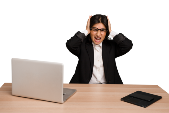 Young indian woman in a table with a laptop and tablet isolated covering ears with hands trying not to hear too loud sound.