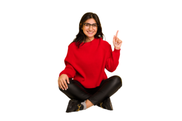 Young indian woman sitting on the floor cut out isolated showing number one with finger.