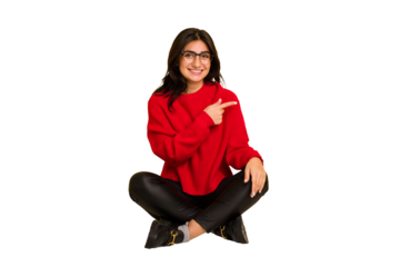 Young indian woman sitting on the floor cut out isolated smiling and pointing aside, showing something at blank space.