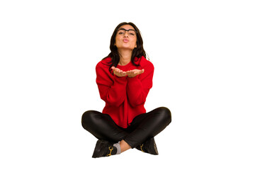 Young indian woman sitting on the floor cut out isolated folding lips and holding palms to send air kiss.