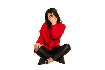 Young indian woman sitting on the floor cut out isolated blink at the camera through fingers, embarrassed covering face.