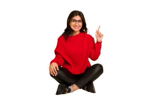 Young indian woman sitting on the floor cut out isolated showing number one with finger.