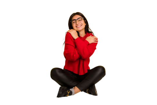 Young indian woman sitting on the floor cut out isolated hugs, smiling carefree and happy.