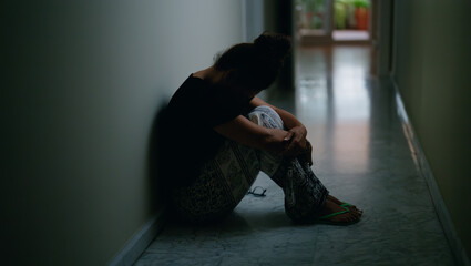 Middle age hispanic woman suffering for domestic violence with bruise on eyes sitting on floor at...