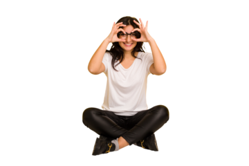 Young indian woman sitting on the floor cut out isolated showing okay sign over eyes