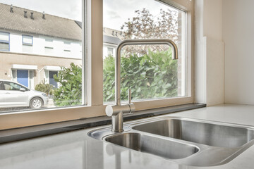 a kitchen sink in front of a window with a view of the street and trees outside, taken from inside