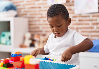 African american boy playing with construction blocks sitting on table at kindergarten