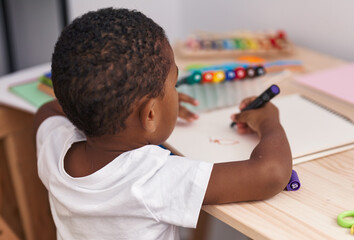 African american boy preschool student sitting on table drawing on notebook at kindergarten