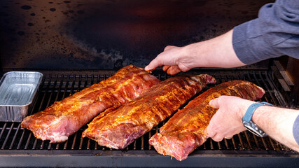 Pit master arranges pork ribs in a smoker