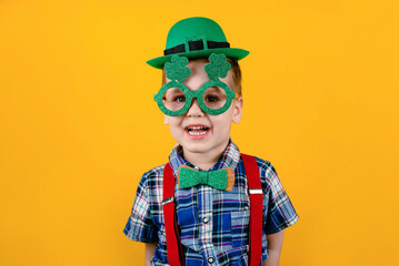 Funny toddler boy with green glasses and a hat on a yellow background. Happy Patrick's Day.