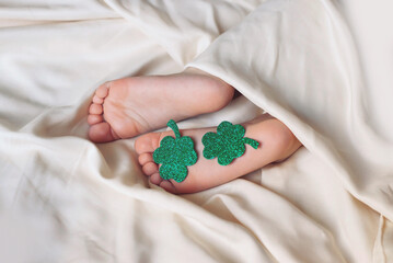 Children's feet and heels on a white bed to Saint Patrick's Day. Infant baby is sleeping in his...