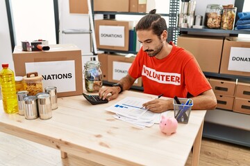Handsome hispanic man working as volunteer calculating donations at donation stand