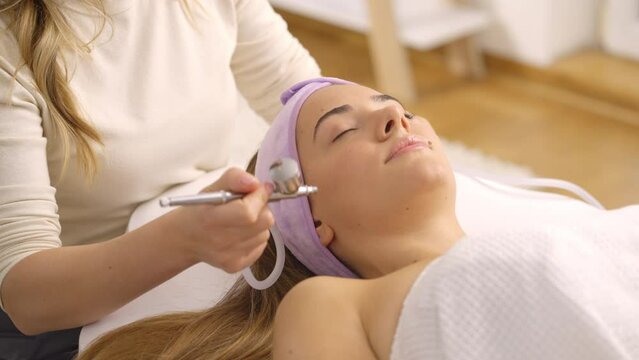 Close-up portrait shot of a young woman getting oxygen infusion facial from professional therapist at spa. Slow-motion shot