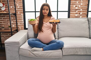 Young pregnant woman craving for food at home relaxed with serious expression on face. simple and...